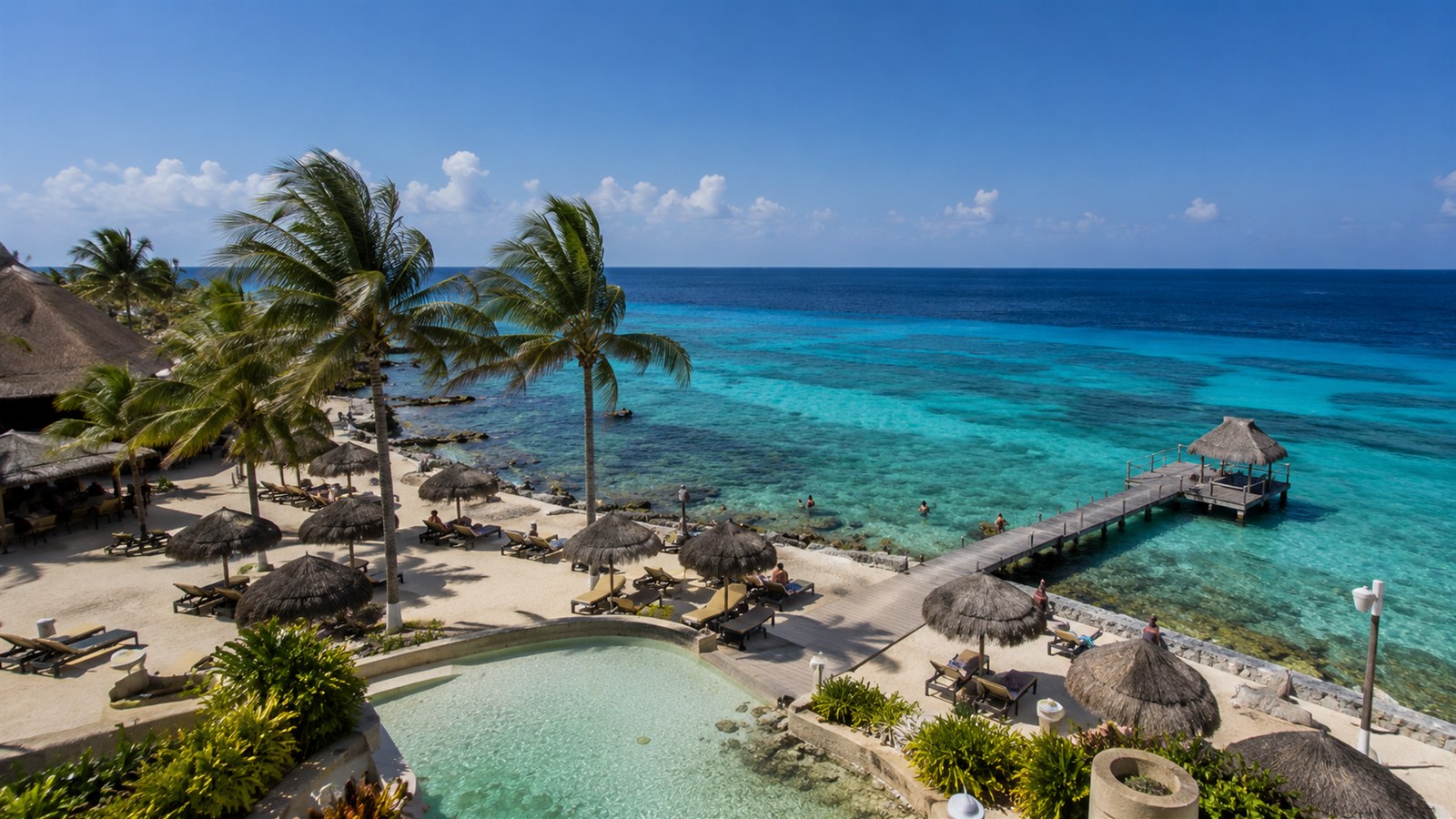 Cozumel beach club with palm trees, loungers, a pier, and clear Caribbean water